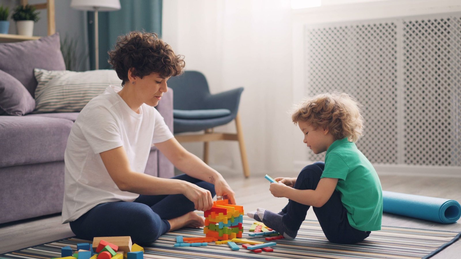 A woman and child engage in playful block building in a cozy living room setting.